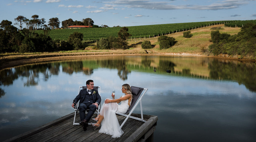 A newly wed couple sit on the deck chairs overlooking the lake, sharing a special moment during their Wills Domain wedding.